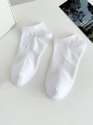 Two white socks on a light gray surface with a magazine in the background.